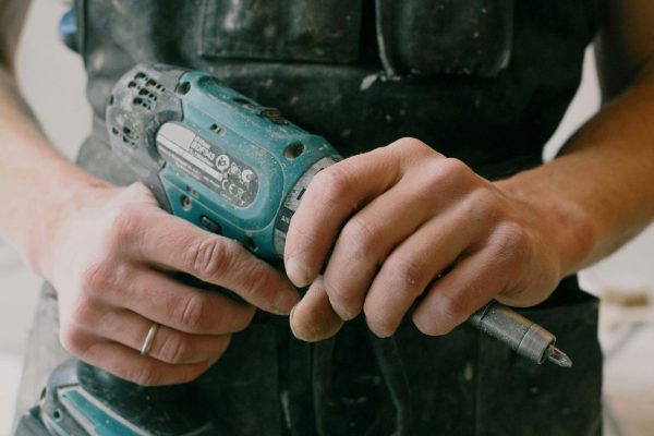 Crop anonymous mechanic in uniform with wireless drill standing in flat during repair works