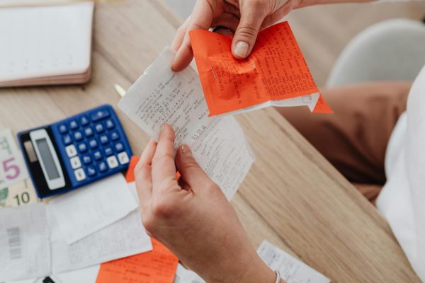 Top view of person organizing finances with calculator, receipts, and notes at desk.
